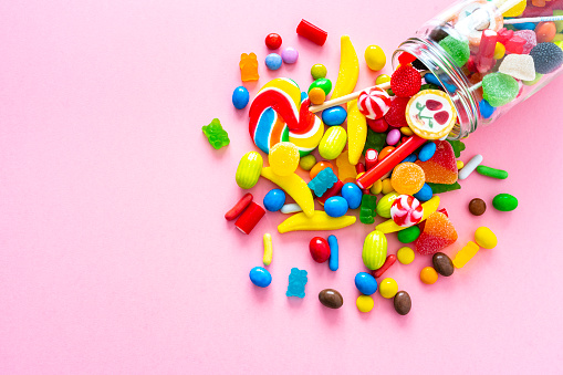 Large group of all sort of multicolored candies spilling out from a glass jar shot from above on pink background. High resolution 42Mp studio digital capture taken with SONY A7rII and Zeiss Batis 40mm F2.0 CF lens