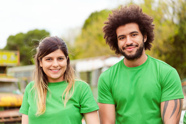 Male and female volunteering for cleanup in park Portrait of smiling male and female volunteers in green t-shirts. Confident environmentalists are in public park. They are volunteering for environmental cleanup. environmentalist stock pictures, royalty-free photos & images