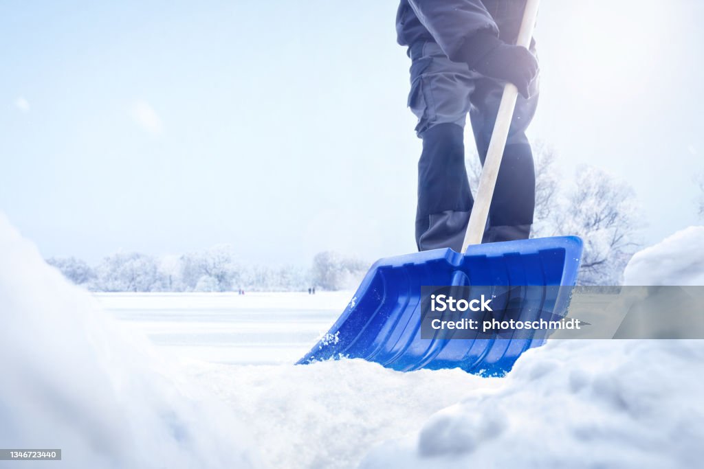 Person using a snow shovel in winter A person using a snow shovel in a snowy landscape. Only the lower part of the person is visible. Low angle shot with snow piles in the foreground. Snow Stock Photo