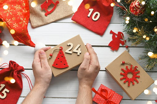 Advent calendar. Merry Christmas. A man's hands hold gift box in kraft paper next to other surprises in bags with numbers for Advent for children. Greeting card or banner for a website. DIY. top view