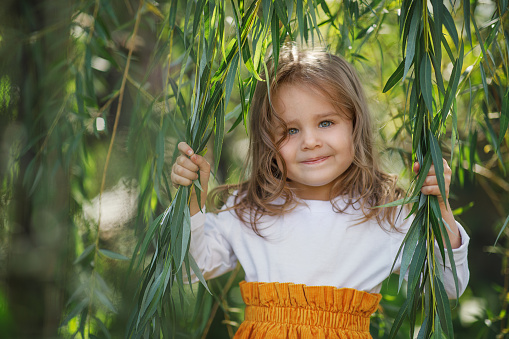Portrait of a girl with blond hair on a background of willow branches. Horizontal photo of people.