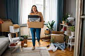Ready to Move out: Happy Caucasian Plus Size Woman Standing in the Middle of a Messy Room while Holding Boxes with Personal Belongings