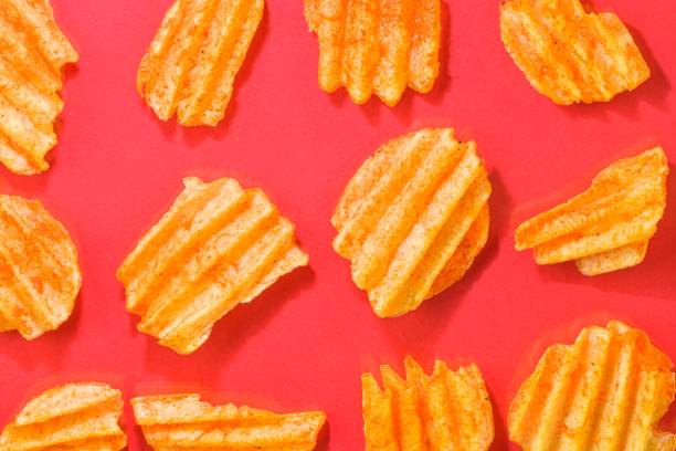 Ribbed potatoes snack with pepper on red background. Ridged potato chips on red background. Set of potato chips. Flat lay. Close-up stock photo