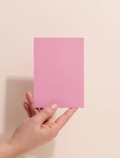 istock Female hand holding empty pink paper on a beige background. Copy paste image or text, close up 1346732834