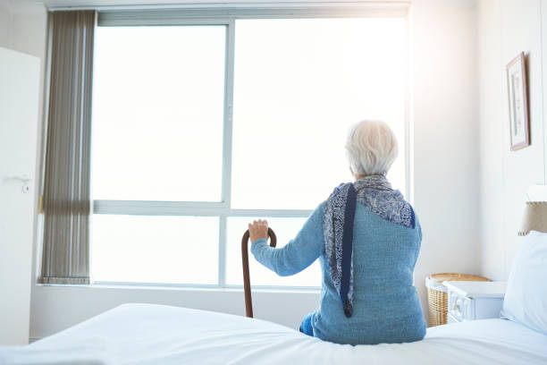 Rearview shot of an unrecognizable senior woman looking thoughtful while sitting in her room at the retirement home stock photo