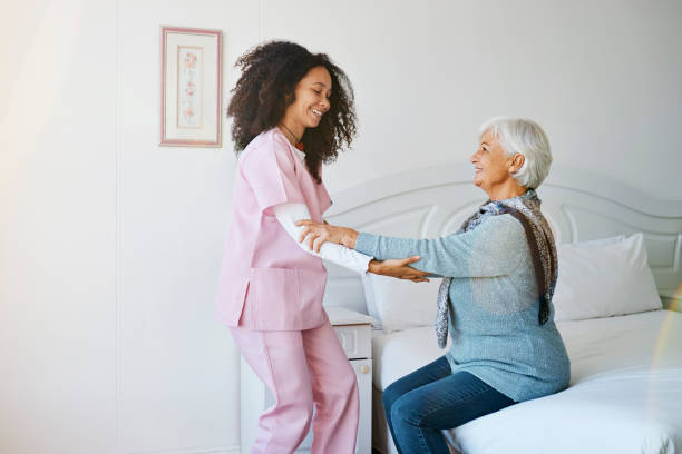 Cropped shot of an attractive young female nurse helping her senior patient off of the bed at the retirement home stock photo