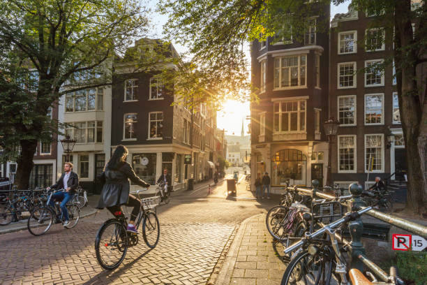 amsterdam, netherlands - september 22, 2021: amsterdam at early morning. artistic image.  people ride bicycles, the ancient european city of amsterdam. sunlight and silhouettes, beautiful downtown houses.  amsterdam, holland, netherlands, europe - grachtenpand stockfoto's en -beelden