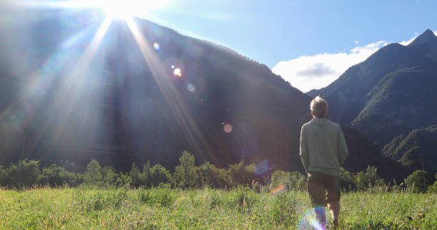 istock Man watches sunrise over distant mountains from lush meadow 1346742461