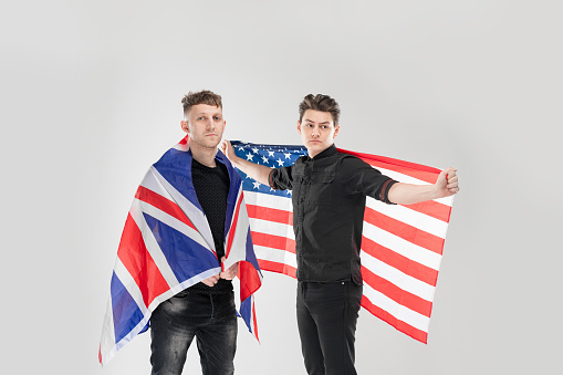 Portrait of two people at the studio with gray background. Concept with copy space. They are holding British and American flags in the hands.