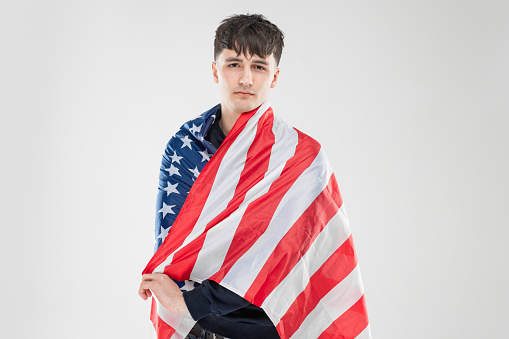 Portrait of one white man at the studio with gray background. Concept with copy space. He is wear black shirt and posing for camera. Picture with American flag