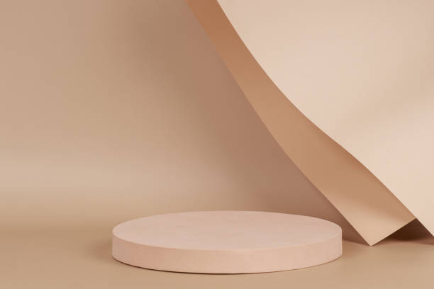 istock Abstract trendy composition with empty round podium platform for product presentation and curve shaped paper on pastel beige background. Front view 1346751518