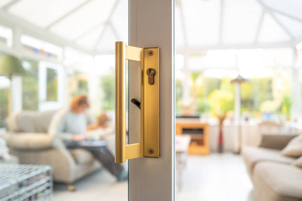 Shallow focus of a gold coloured handle seen on opened patio doors. Shallow focus of a gold coloured handle seen on opened patio doors. Leading to a large conservatory seen with a person and sitting dog. patio doors stock pictures, royalty-free photos & images