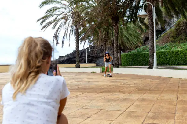 Two teenagers outdoors filming on the mobile phone a skate video to publish on social media accounts