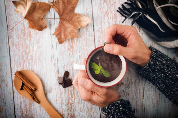 kalte hände rühren heiße schokolade in einer tasse auf dem tisch - hot chocolate hot drink high section color image stock-fotos und bilder