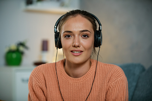 Personal perspective shot of young female university student wearing headphones and smiling at camera as is she is on a video conference call, attending online class.