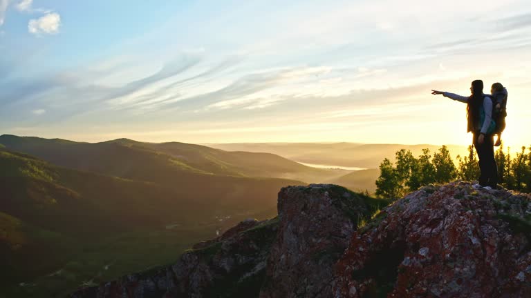 Drone shot of a young mother with her young son in a carrier hiking on a mountain trail at sunset