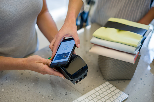 Close-up on a woman making a contactless payment at a furniture store with her cell phone. **DESIGN ON SCREEN BELONGS TO US**