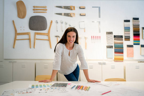Happy interior designer working the office and smiling Happy female interior designer working the office and looking at the camera smiling. **DESIGN OF DOCUMENTS ON TABLE BELONG TO US** interior designer stock pictures, royalty-free photos & images