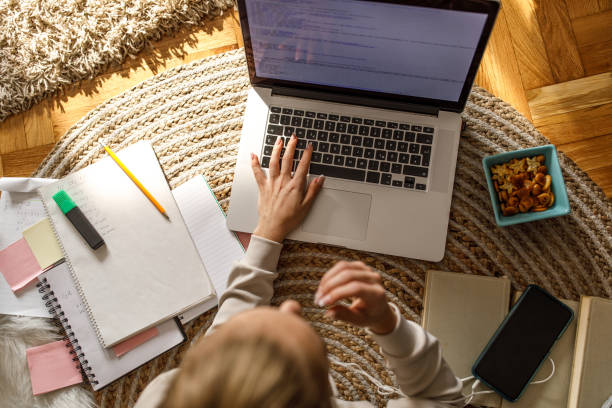 istock Teenage girl snacking while typing homework on laptop 1346781809