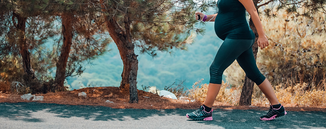 Sportive Pregnant Woman Jogging in the Mountainous Forest in Sunny Day. Enjoying the Walk Among Fresh Pine Trees. Body Part. Healthy Pregnancy.