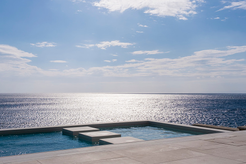 Luxury modern minimalist house exterior with infinity swimming pool and beautiful sea and ocean view. Poster template background for Real estate, tourism hotel, home and villa vacation rental with large copy space.