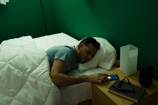 Alarm sounds. Sleepy and tired man turning off his alarm on the smartphone early in the morning