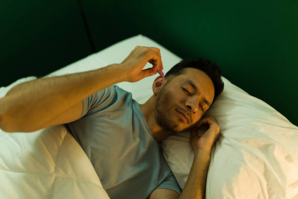 Hispanic man likes to sleep with no sound Attractive latin man with sleeping problems putting on ear plugs before sleeping at night ear plug stock pictures, royalty-free photos & images