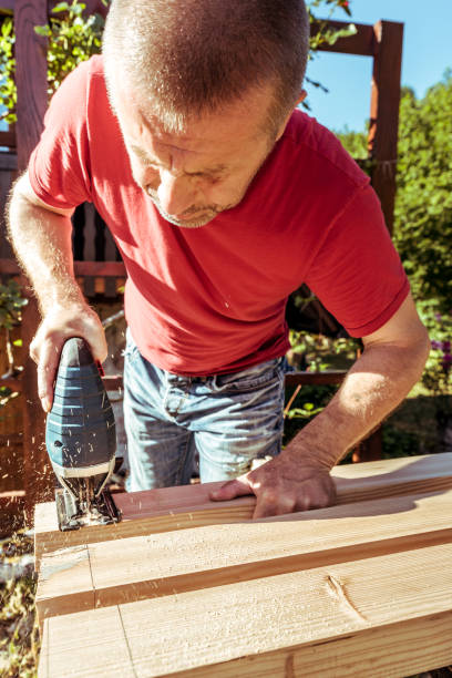 istock Man Sawing Raw Wooden Fence Board Using Electric Jigsaw 1346784981