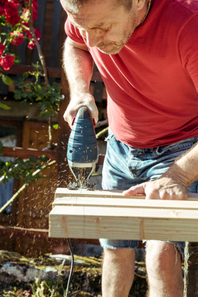 istock Man Sawing Raw Wooden Fence Board Using Electric Jigsaw 1346784982