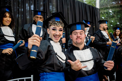 Portrait of two graduates on graduation day. A non-binary person and a man with down syndrome