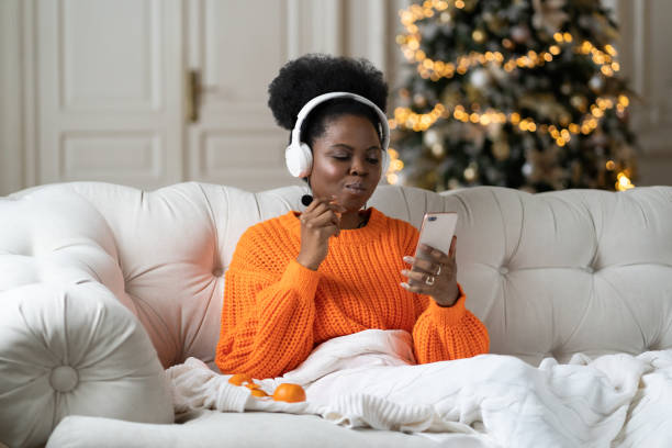 femme africaine passer le matin de noël à la maison dans le salon avec arbre de noël lire des sms dans smartphone - christmas tree audio photos et images de collection