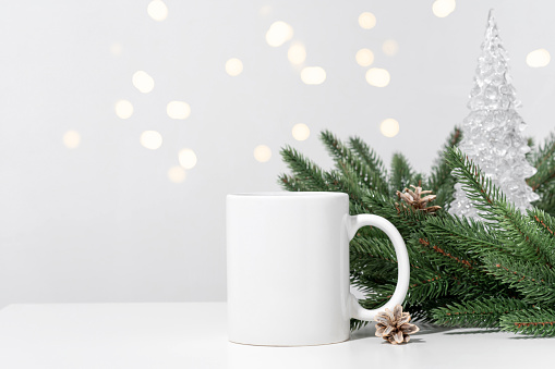 Christmas mockup one white empty tea mugs on a white table and branches of a Christmas tree wreath. Cup template for your design, logo with copy space. New Year