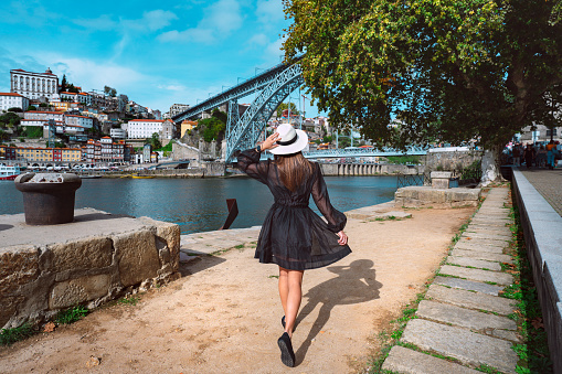 Young woman tourist in black dress enjoying beautiful view of Porto city and famous famous Dom Luis I Bridge. Summer holiday vacation in North Portugal. High quality photo