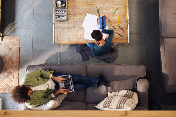 istock Overhead of man using laptop and boy drawing 1346794853