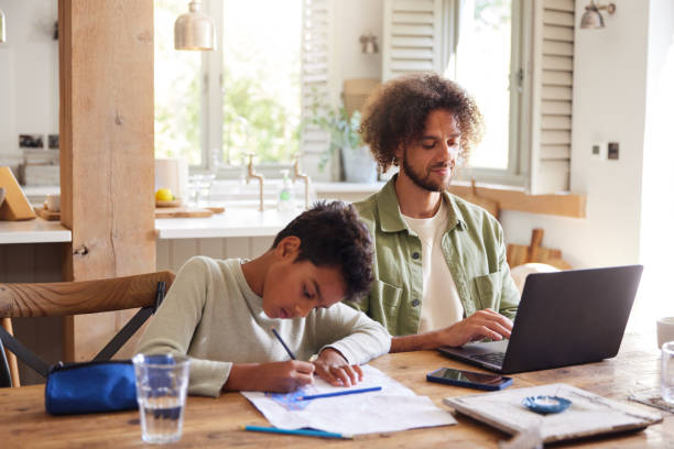 istock Father using laptop with son drawing at home 1346794911