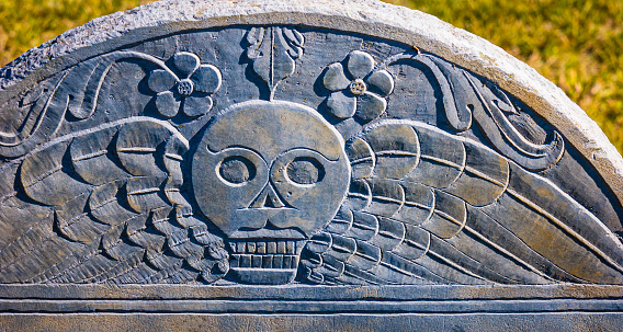 Close up of an ancient 18th century gravestone carving of a winged skull with flowers representing death and life.