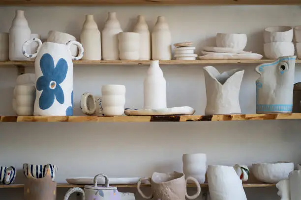 Photo of Handicraft ceramic crockery, craft pottery tableware on shelves in creative studio or potter store