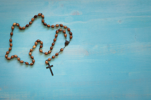 Wood rosary prayer beads with dark metal crucifix on a blue wood background with copy space