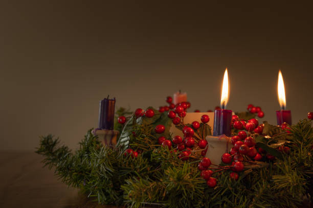 Advent wreath with two candles lit Advent wreath with evergreen boughs and red berries with two purple candles lit shot from tabletop with copy space week photos stock pictures, royalty-free photos & images
