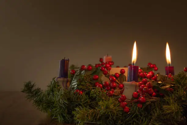 Advent wreath with evergreen boughs and red berries with two purple candles lit shot from tabletop with copy space