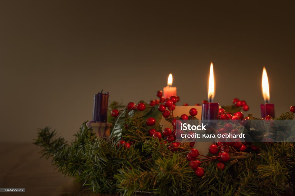 Advent wreath with three candles lit Advent wreath with evergreen boughs and red berries with three candles lit shot from tabletop with copy space Advent Stock Photo