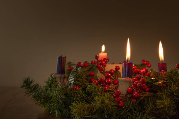 Advent wreath with three candles lit Advent wreath with evergreen boughs and red berries with three candles lit shot from tabletop with copy space advent photos stock pictures, royalty-free photos & images