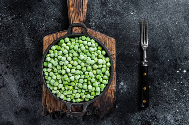 istock Fresh Frozen green peas in a pan. Black background. Top view 1346802598