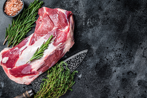 Fresh Raw lamb mutton shoulder meat with butcher knife. Black background. Top view. Copy space.