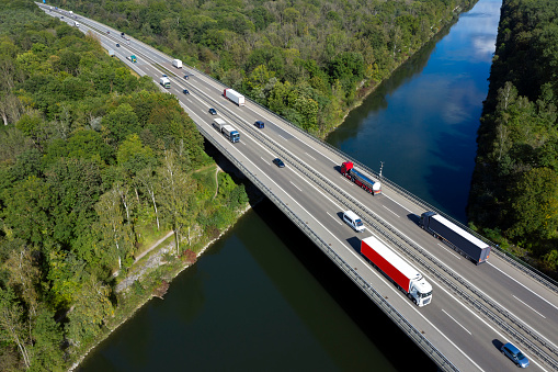 Aerial view of a truck and car traffic on a highway bridge over a river.