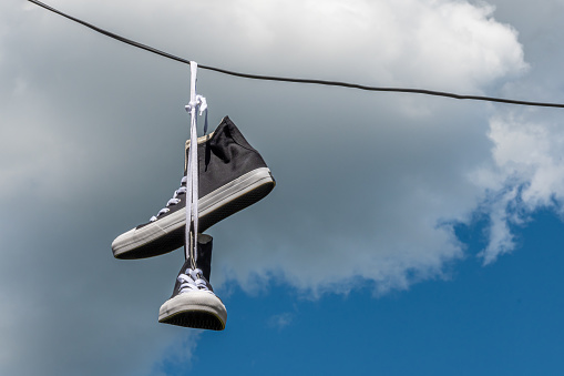 Sneakers hanging on electric wires against a background of blue sky and white clouds.