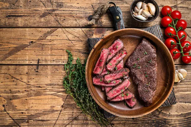 Grilled sliced top blade or denver beef meat steak in a wooden plate with herbs. wooden background. Top view. Copy space.