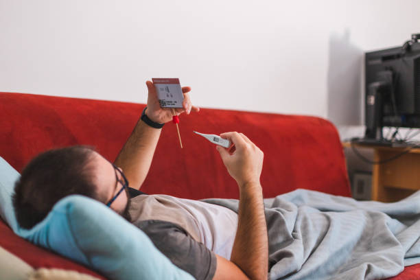 istock Ill young man holding a COVID-19 rapid self-test kit showing that he is Coronavirus positive and a thermometer while laying in bed at home 1346810178