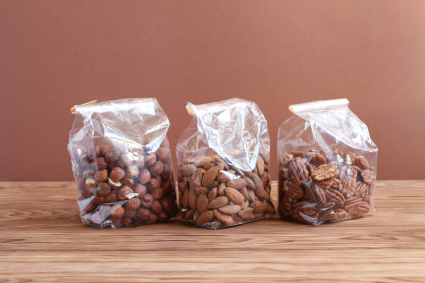 istock Three types of nuts - hazelnuts, almonds, pecan nuts - in transparent bags on a wooden table against a brown wall. Closeup 1346818048