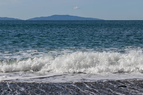 istock Waves on the beach with mountains on the horizon 1346825086
